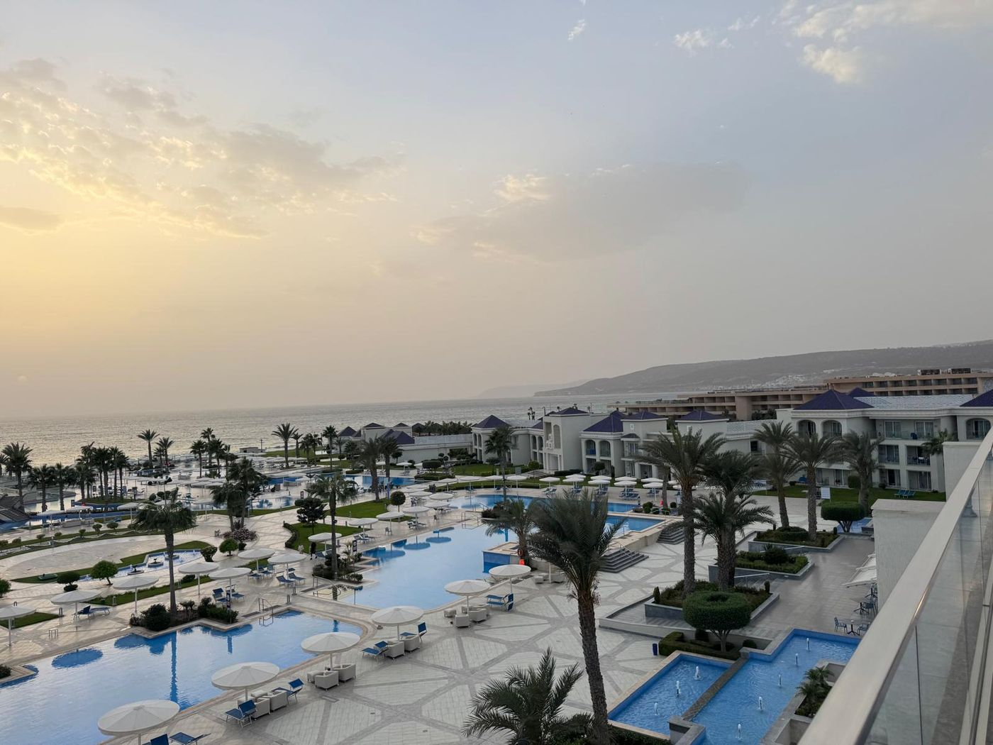 Palm-lined pools and white resort buildings beside the Atlantic at sunset in Agadir, Morocco